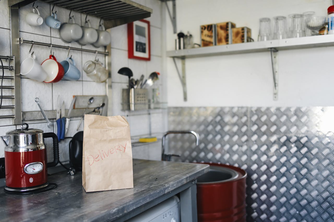 A home kitchen setting with a paper delivery bag on the counter, surrounded by kitchenware and appliances.